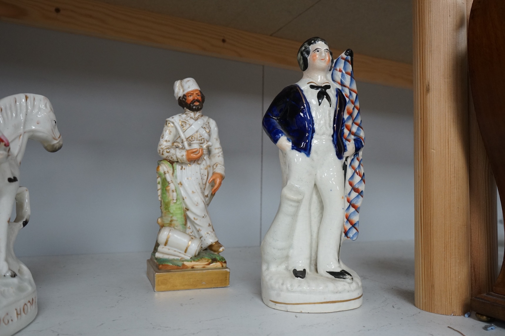 A mid 19th century Paris porcelain figure of a Turkish soldier and six pieces of staffordshire including ‘The Death of Nelson’ group, a 19th century British sailor, ‘Returning Home’ group, and three buildings, tallest 23